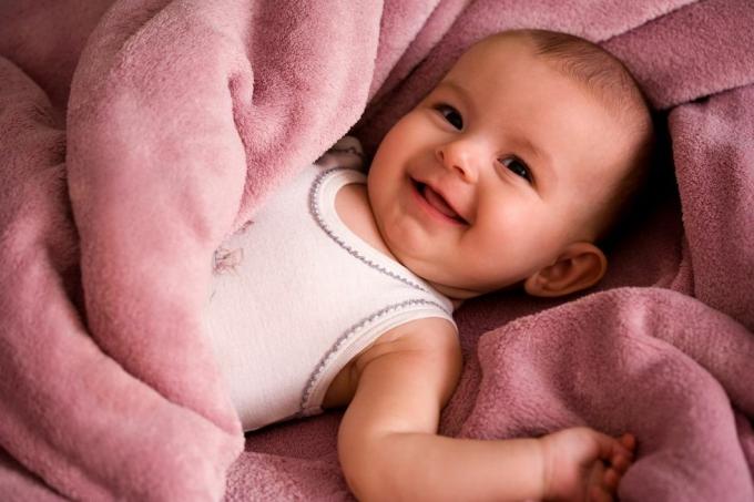portret bebe u bijeloj majici u stilu tanke nasmijane i umotane u nježno ružičastu dekicu