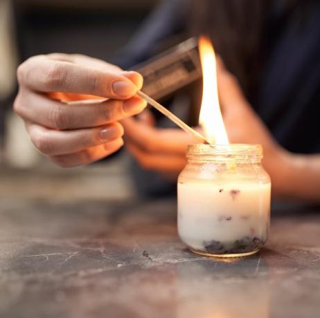 obrezivanje anonimna žena s gorućom šibicom paljenje aromatične svijeće u staklenoj posudi postavljenoj na mramorni stol kod kuće