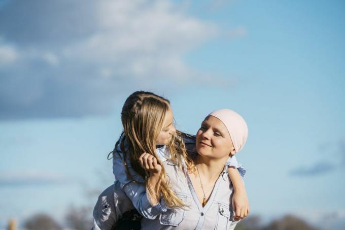 žena viđena od brade do trbuha kako pruža ruke kako bi napravila oblik srca kako bi uokvirila ružičastu vrpcu na svom bijelom džemperu