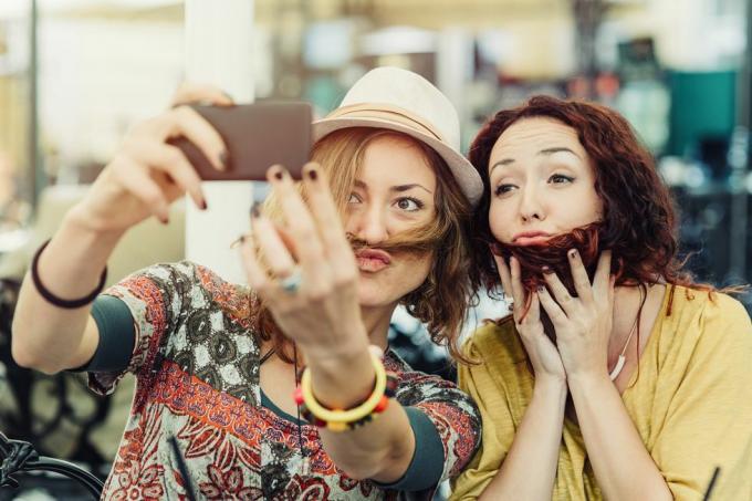 dvije djevojke drže kosu preko lica da izgledaju kao da imaju bradu i brkove i snimaju selfie toga