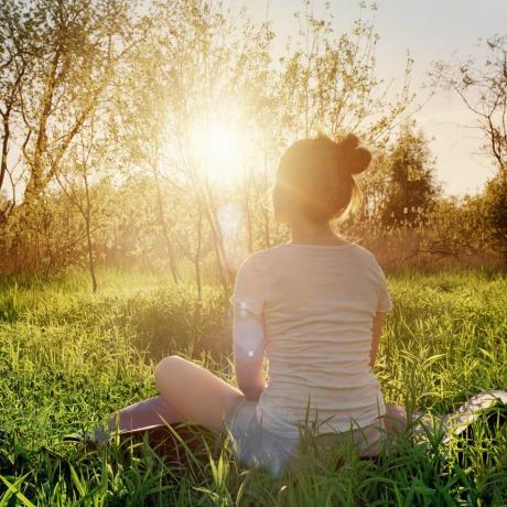 mlada žena sjedi u položaju joge i uživa u zalasku sunca u prirodi